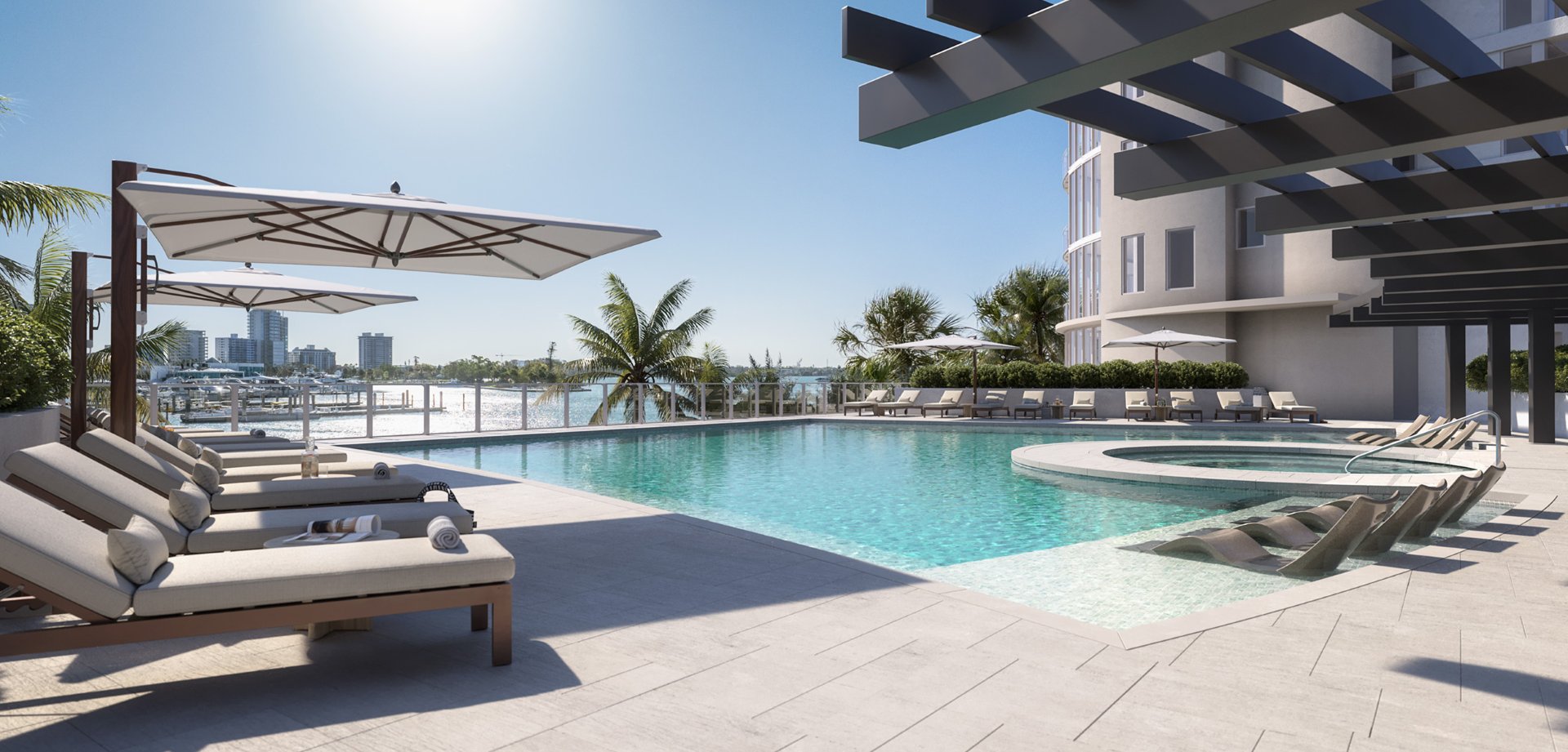 Resort-style pool at Amara on Sarasota Bay with in-water loungers, shaded seating, palm trees, and bay views overlooking the waterfront.