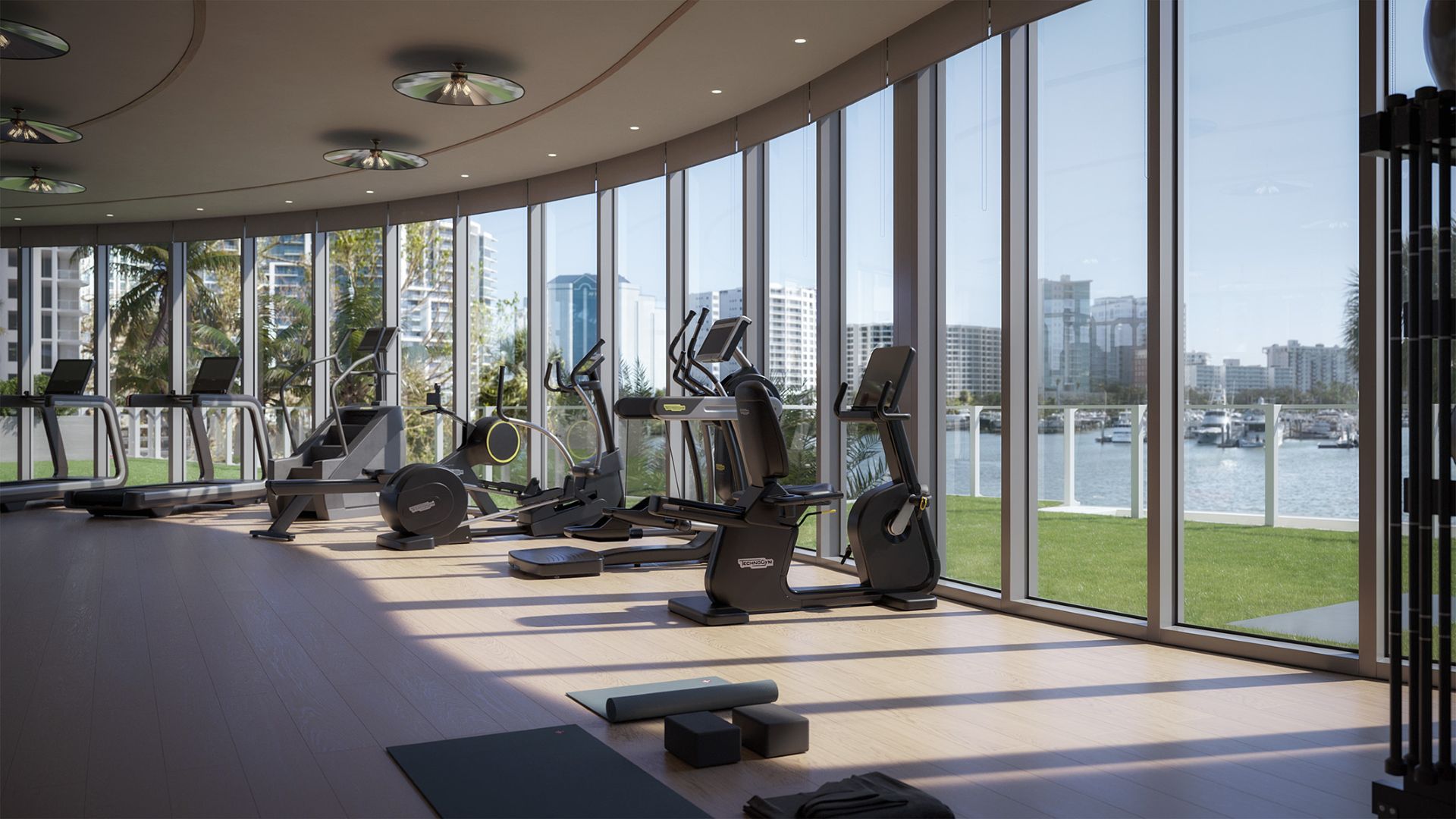 Fitness center at Amara on Sarasota Bay featuring modern exercise equipment, floor-to-ceiling windows, and views of the bay and surrounding waterfront.
