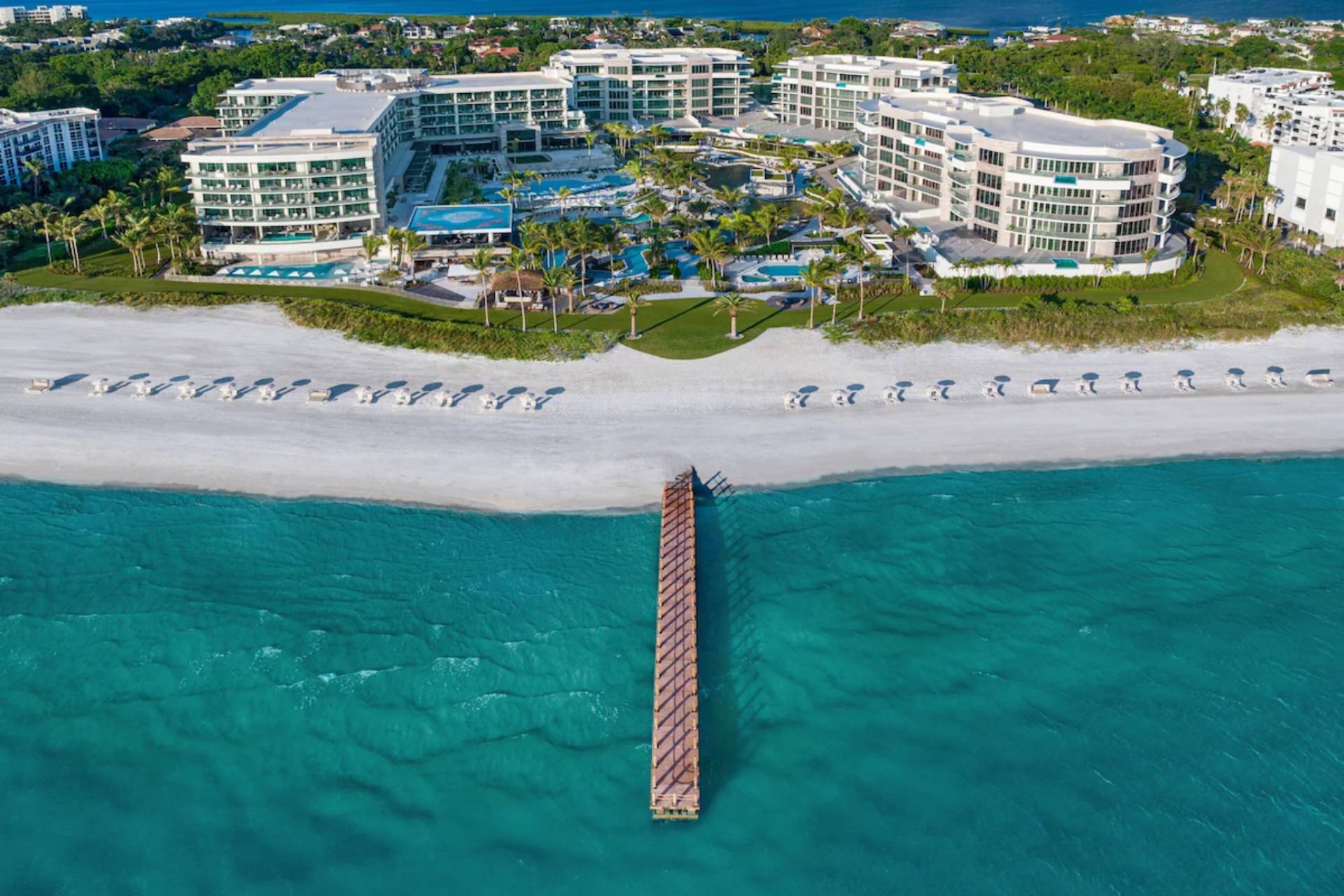 Aerial view of St. Regis Longboat Key featuring oceanfront buildings, white-sand beach, private pier, and the Gulf of Mexico.