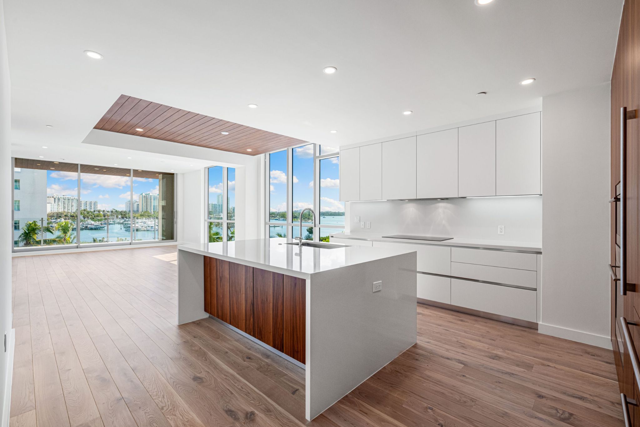 Luxury open kitchen with white cabinetry, wood flooring, and floor-to-ceiling windows framing Sarasota Bay views