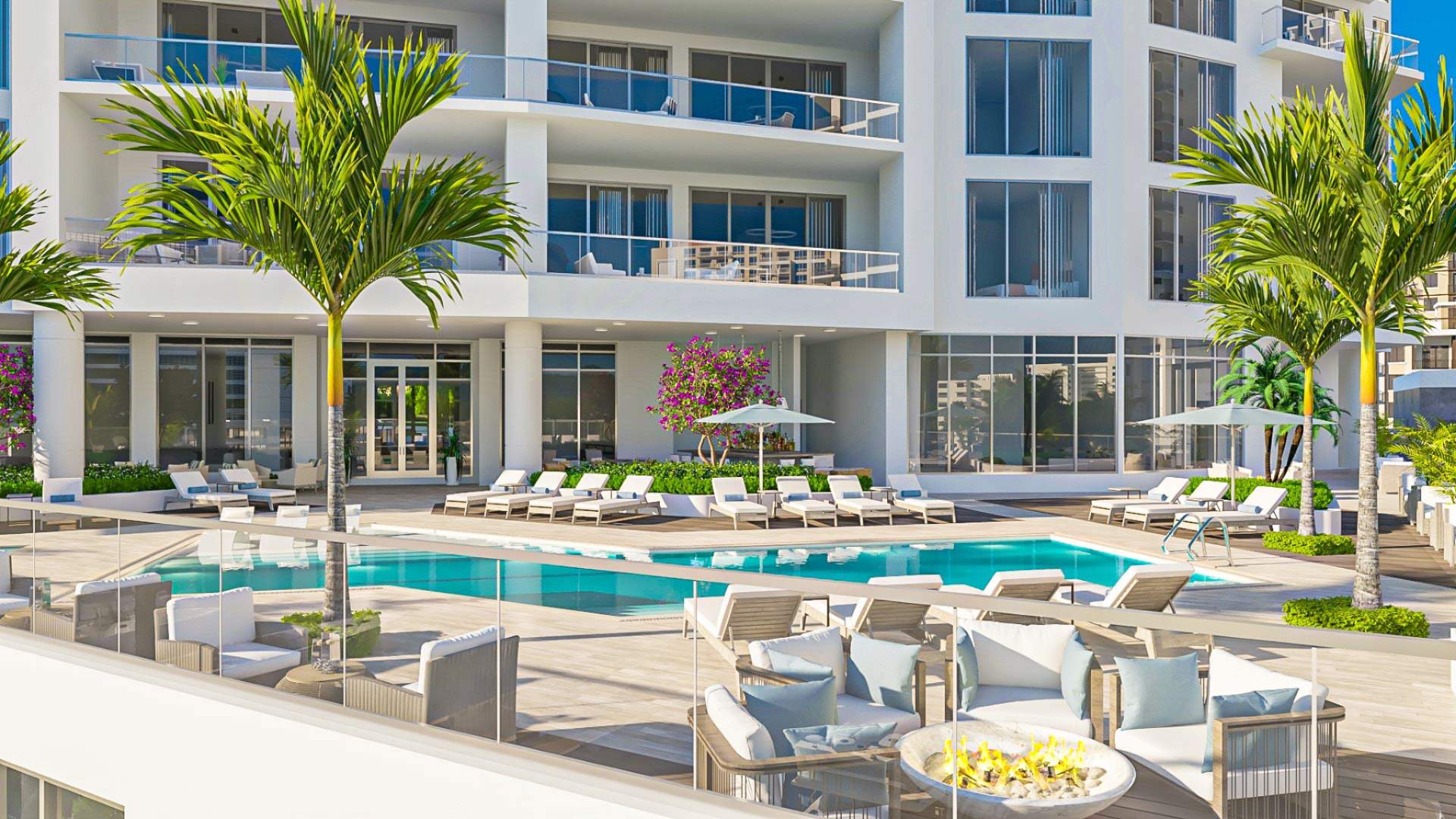 Elevated resort-style pool terrace at The Ritz-Carlton Residences Sarasota Bay featuring luxury loungers, fire pit seating, palm trees, and waterfront views.