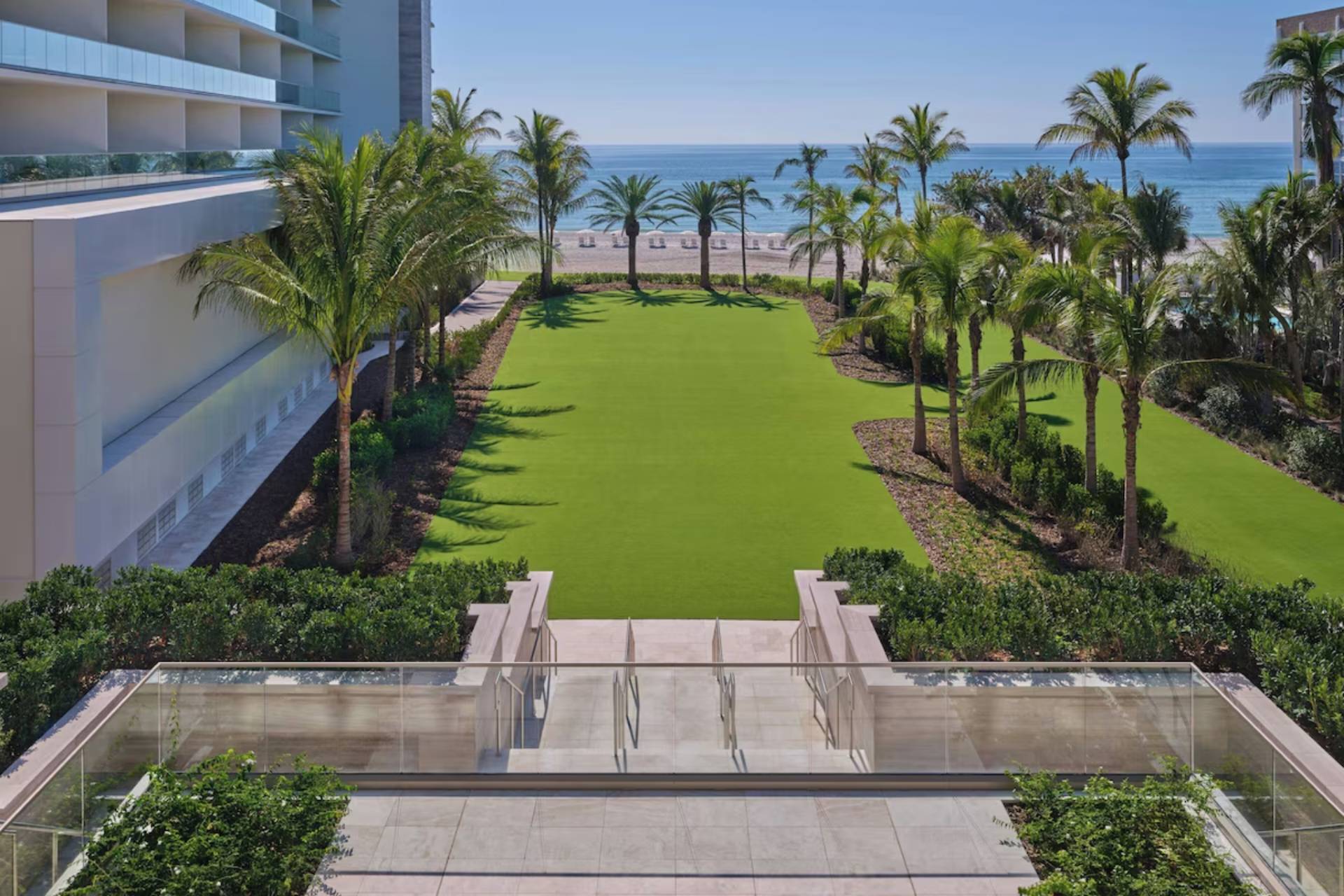 Manicured oceanfront lawn framed by palm trees and pathways with direct access to the beach at St. Regis Residences Longboat Key.