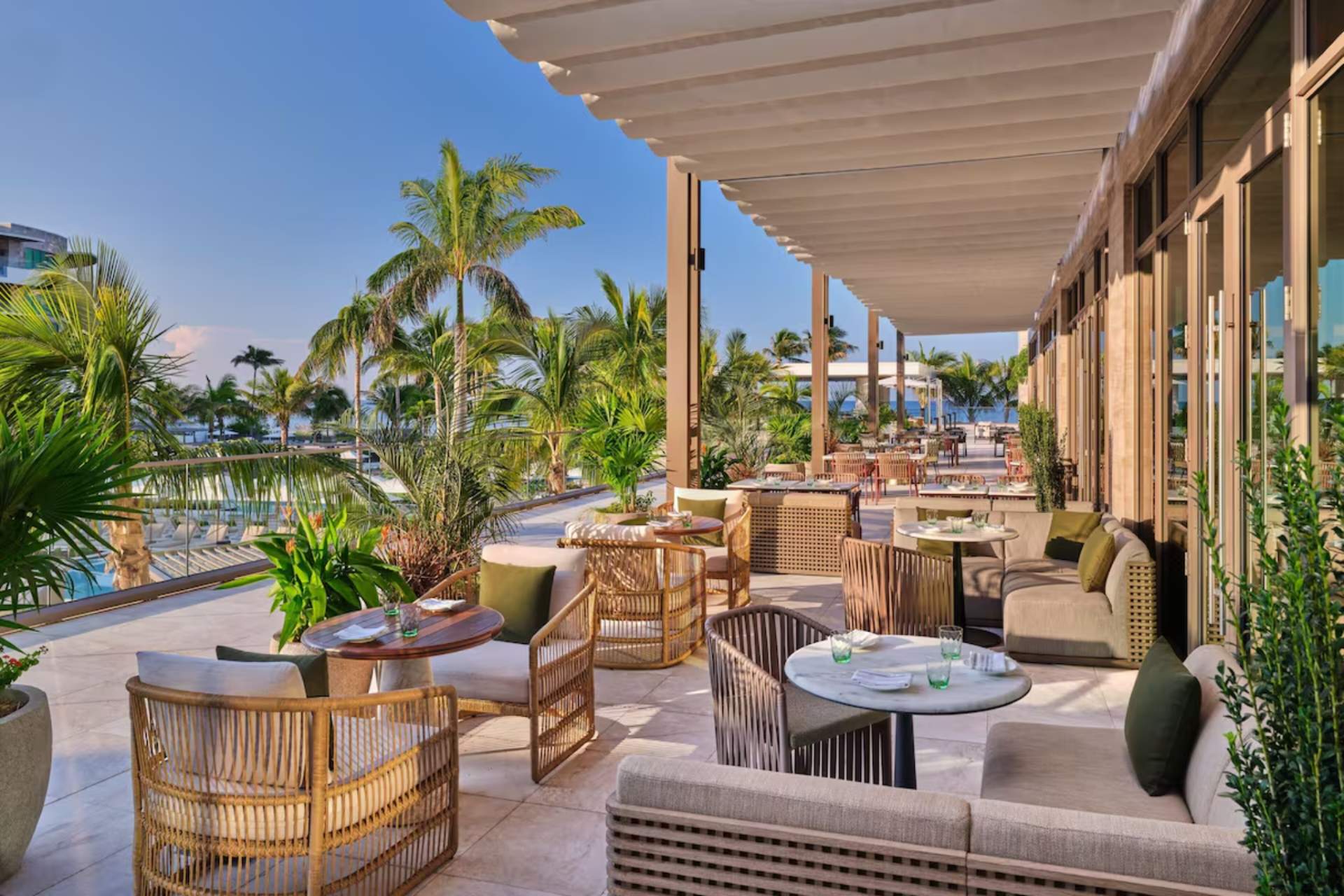 Open-air oceanfront terrace with lounge seating and dining tables surrounded by palm trees at St. Regis Residences Longboat Key.