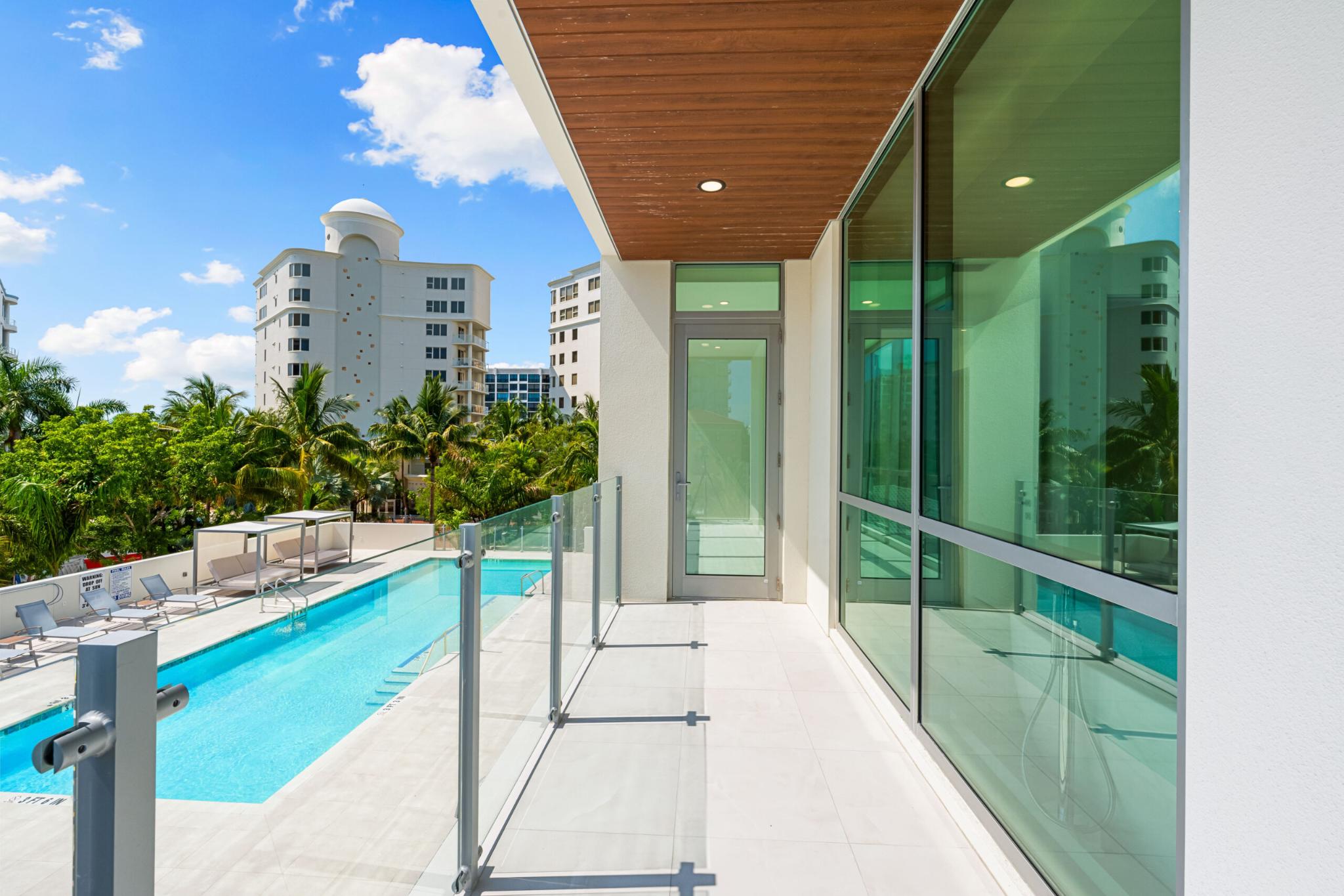 Glass-railed balcony with modern architecture and views of the building’s pool deck and surrounding palm trees