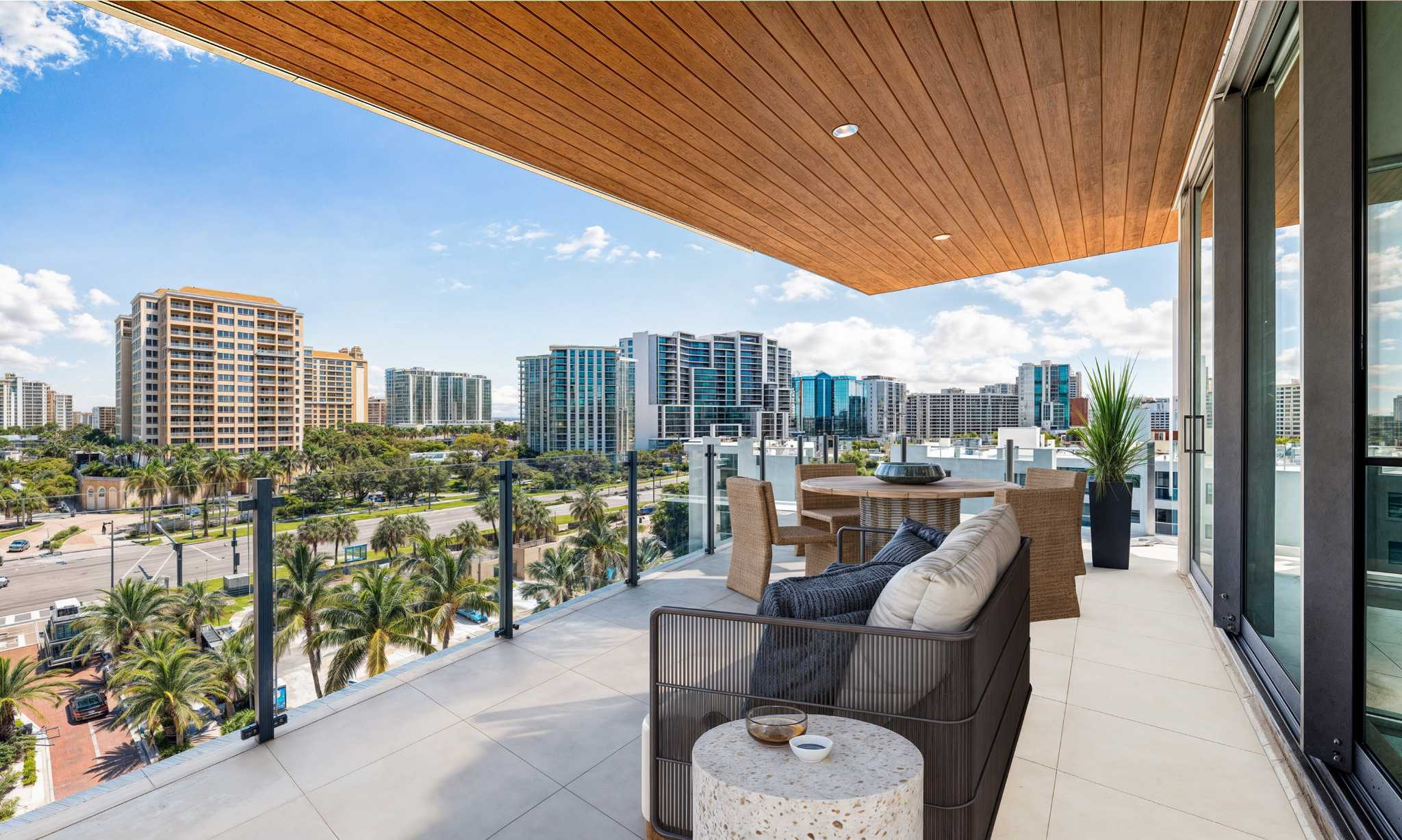 Spacious balcony with outdoor seating and glass railing overlooking Sarasota skyline and palm-lined streets