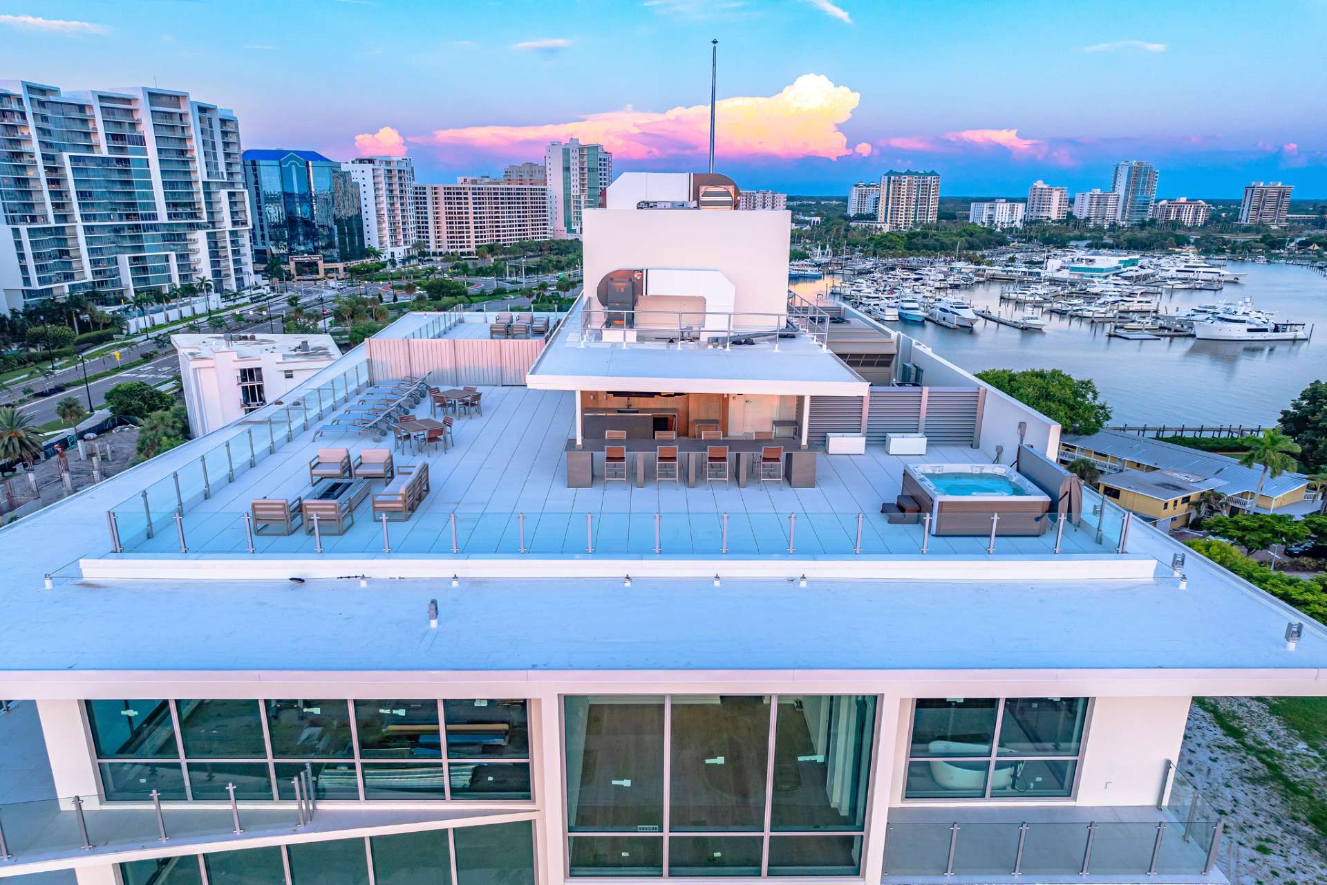 Aerial view of The Evolution rooftop terrace featuring outdoor kitchen, spa, lounge seating, and panoramic marina and sunset views over Sarasota Bay