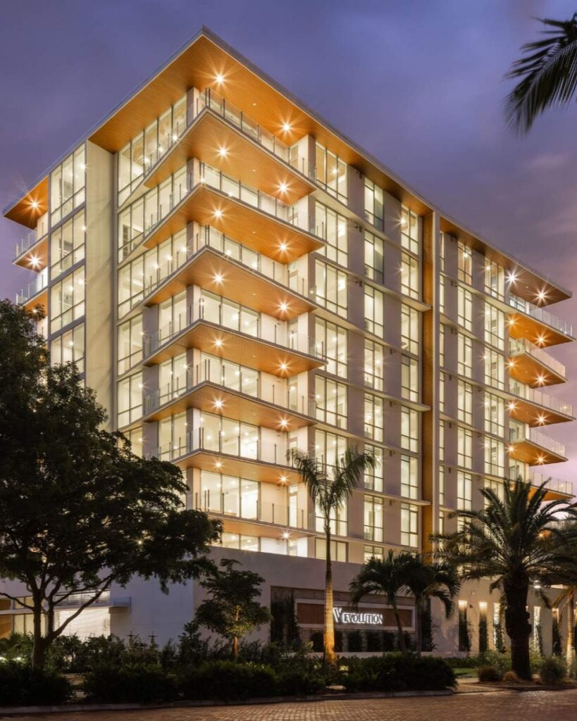 Evening exterior view of The Evolution luxury condominium with illuminated glass balconies and contemporary architecture in Sarasota