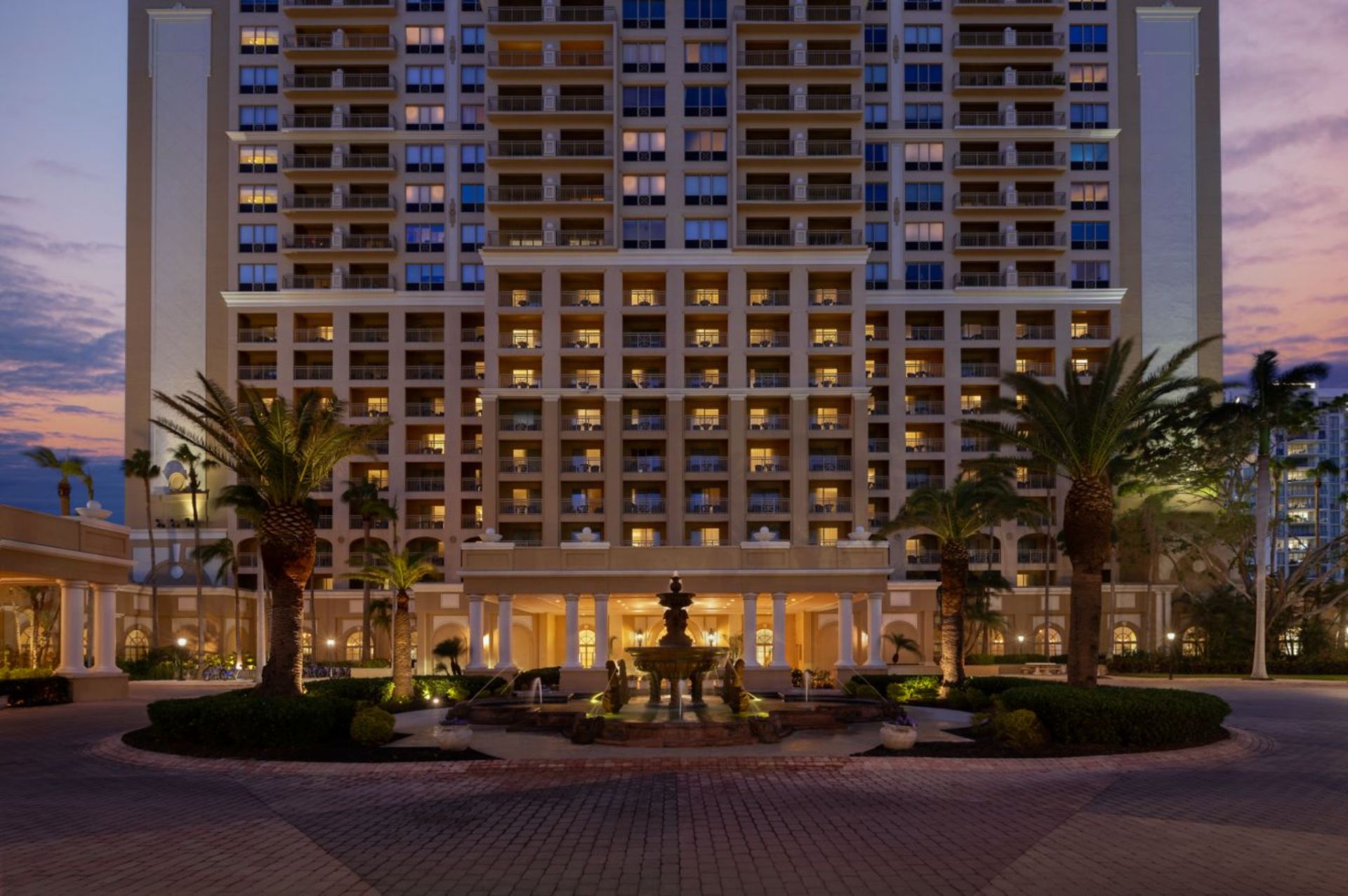 Elegant front entrance with fountain and palm-lined driveway at The Ritz-Carlton Sarasota at dusk