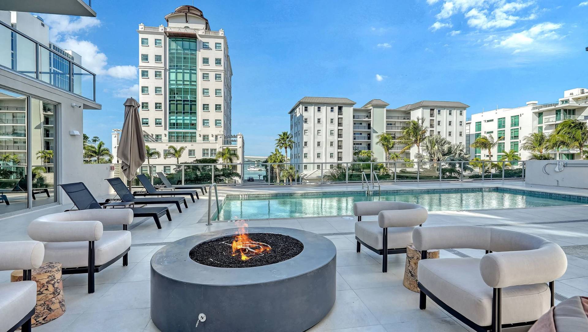 Modern outdoor seating area with fire pit beside pool at Peninsula Sarasota overlooking Sarasota skyline