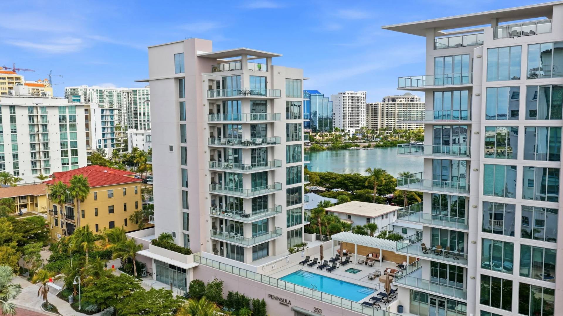Aerial view of Peninsula Sarasota luxury waterfront condo buildings with resort-style pool and Sarasota Bay in the background