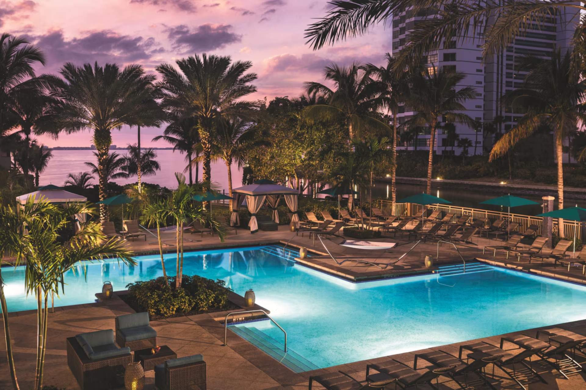 Illuminated resort-style pool with cabanas and palm trees at The Ritz-Carlton Sarasota at dusk