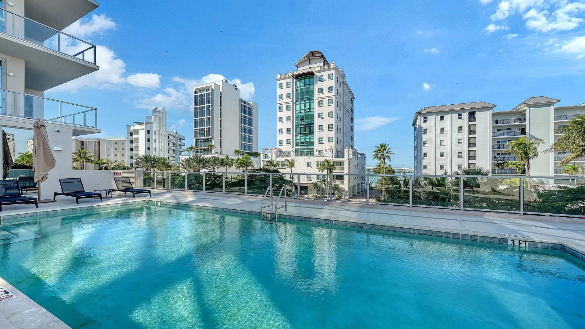 Luxury pool deck with lounge chairs and city skyline views at Peninsula Sarasota waterfront residences