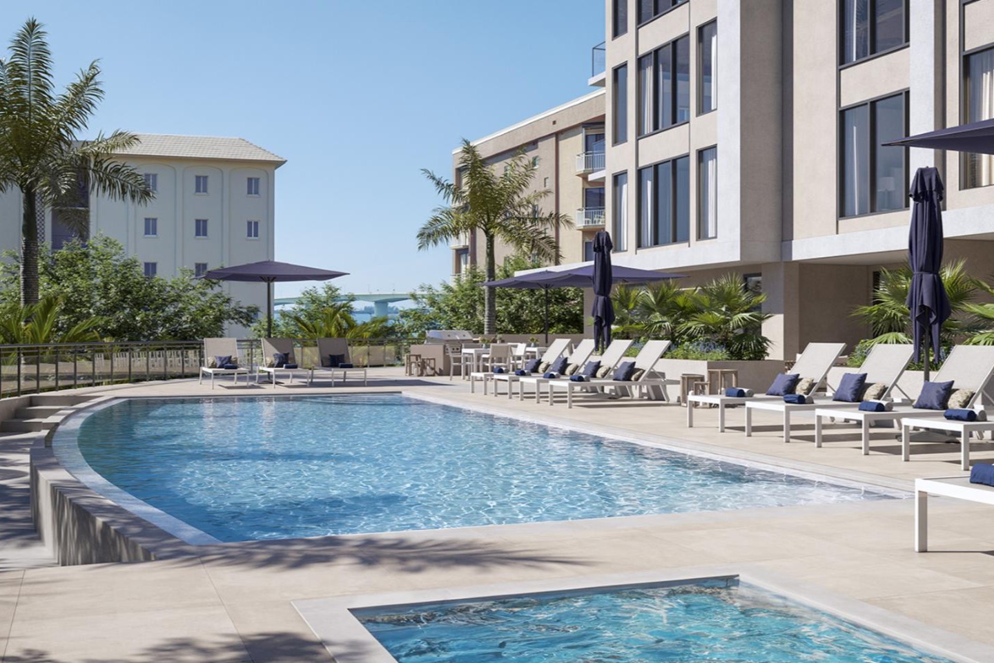 Resort-style pool at The Owen Sarasota with expansive sundeck, lounge chairs, umbrellas, and tropical landscaping.