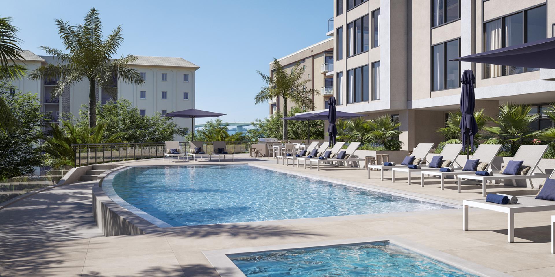 Resort-style pool at The Owen Sarasota with expansive sundeck, lounge chairs, umbrellas, and tropical landscaping.