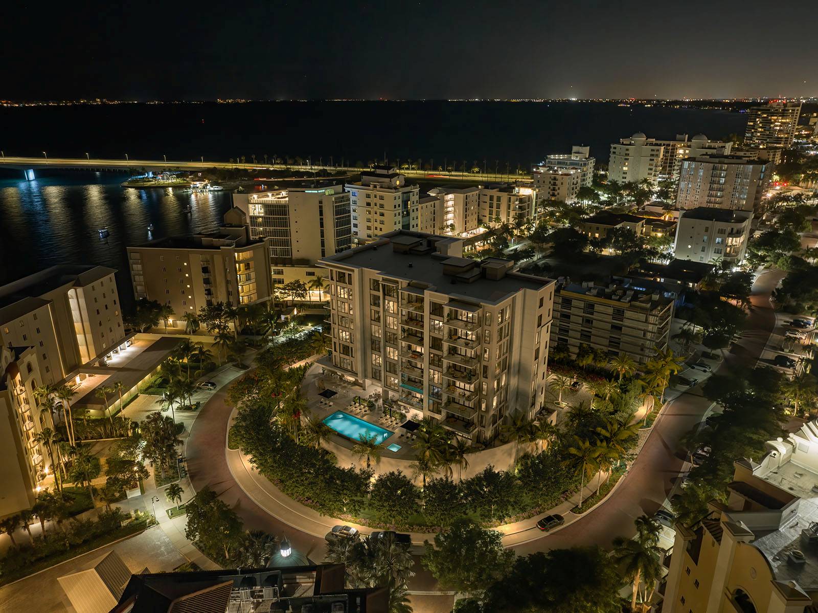 Aerial night view of The Owen illuminated with pool deck and surrounding Golden Gate Point waterfront in Sarasota.