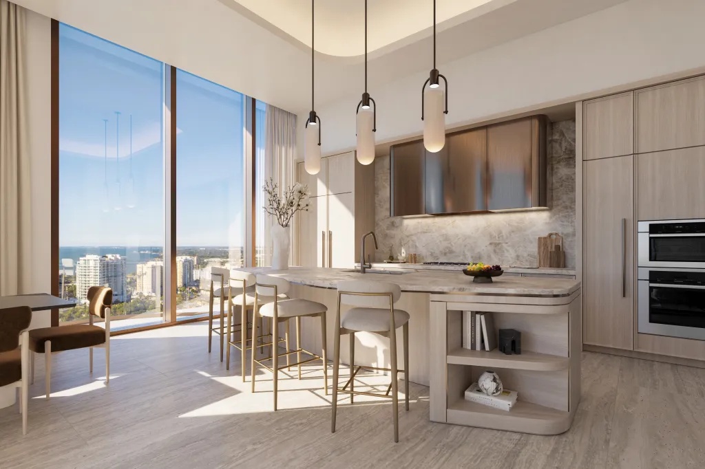 Modern luxury kitchen at Waldorf Astoria Residences Sarasota featuring marble island, custom cabinetry, pendant lighting, and floor-to-ceiling windows overlooking Sarasota Bay