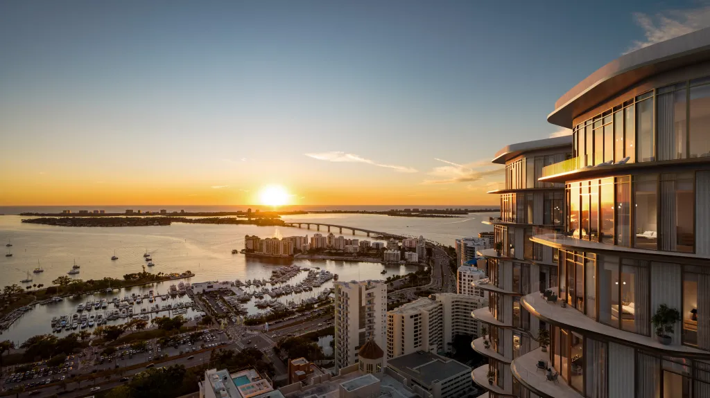 Sunset view from Waldorf Astoria Residences Sarasota featuring Sarasota Bay, marina, and city skyline with curved glass tower architecture and golden reflections