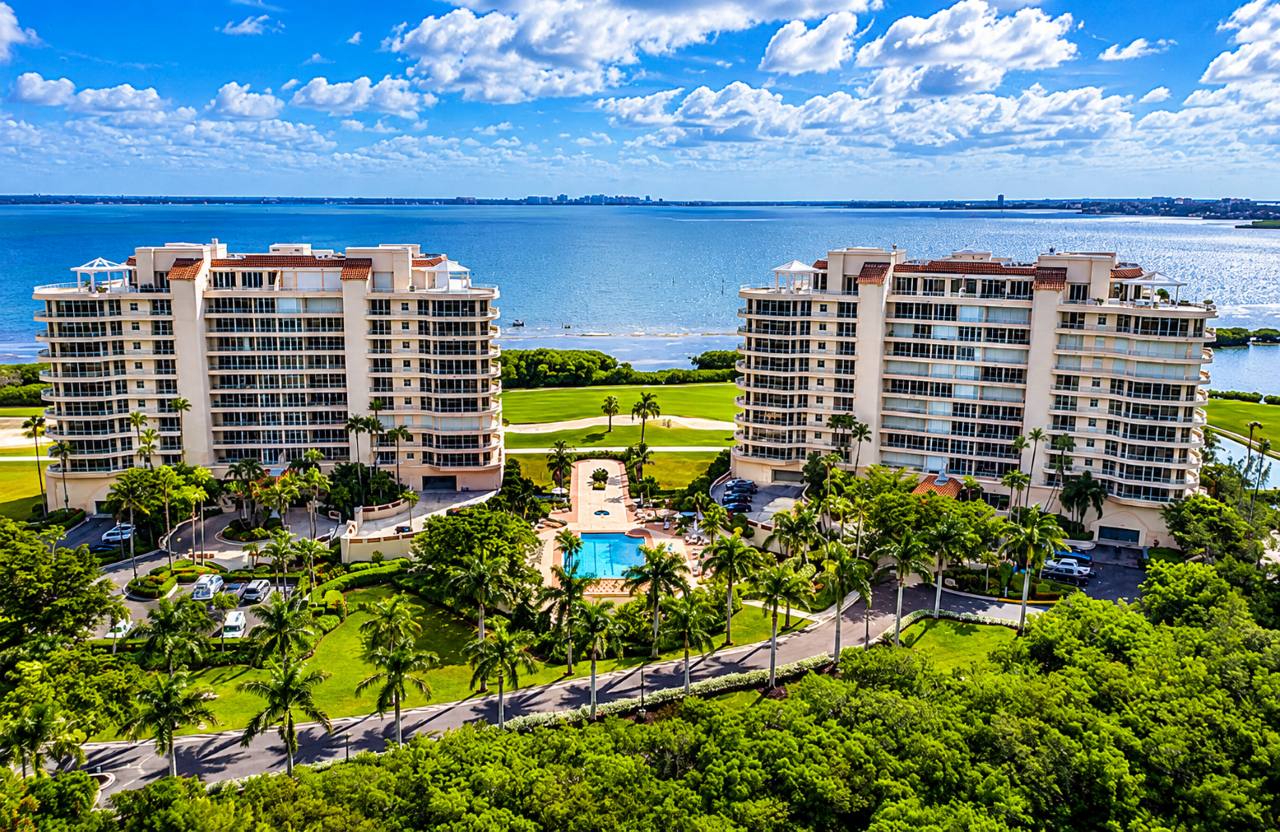 Aerial view of Grand Bay Longboat Key condominium residences, resort-style pool, tropical landscaping, and Sarasota Bay.