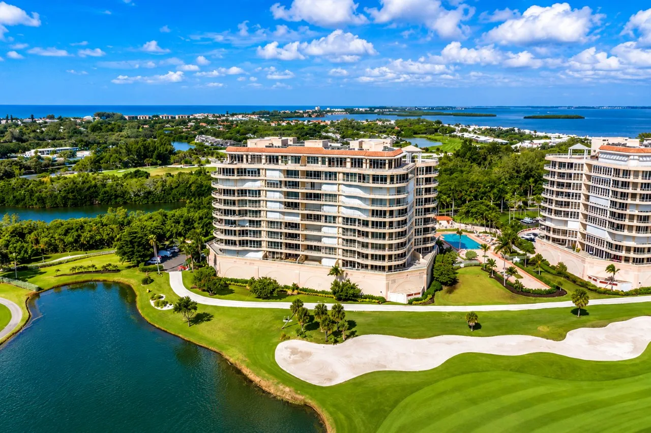 Aerial view of Grand Bay Longboat Key residences overlooking the Harbourside golf course, lagoon, resort-style pool, and surrounding coastal landscape.
