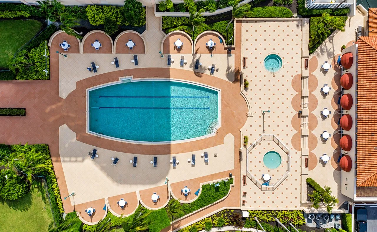 Aerial view of the resort-style swimming pool, spa areas, lounge seating, and tropical landscaping at Grand Bay on Longboat Key, Florida.